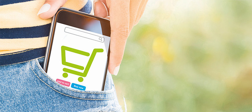 Eine Bild von einer Person die ein Smartphone aus Ihrer Tasche zieht, auf dem Smartphone ist das Zeichen eines Einkaufswagens, was den Onlinehandel symbolisieren sol