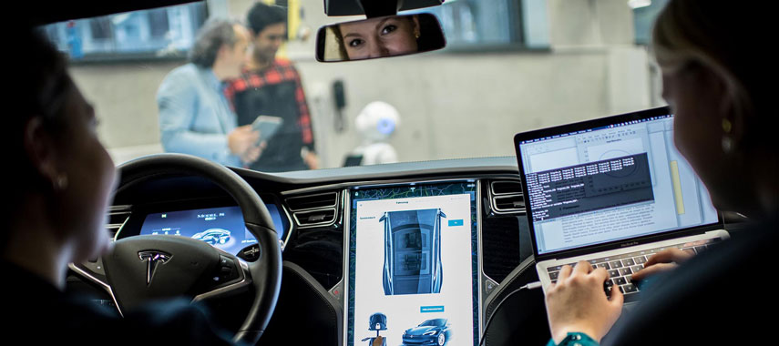 Ein Bild von zwei Personen, die in einem Auto sitzen vor ihnen sind zwei weitere Personen, die mit einem Roboter arbeiten